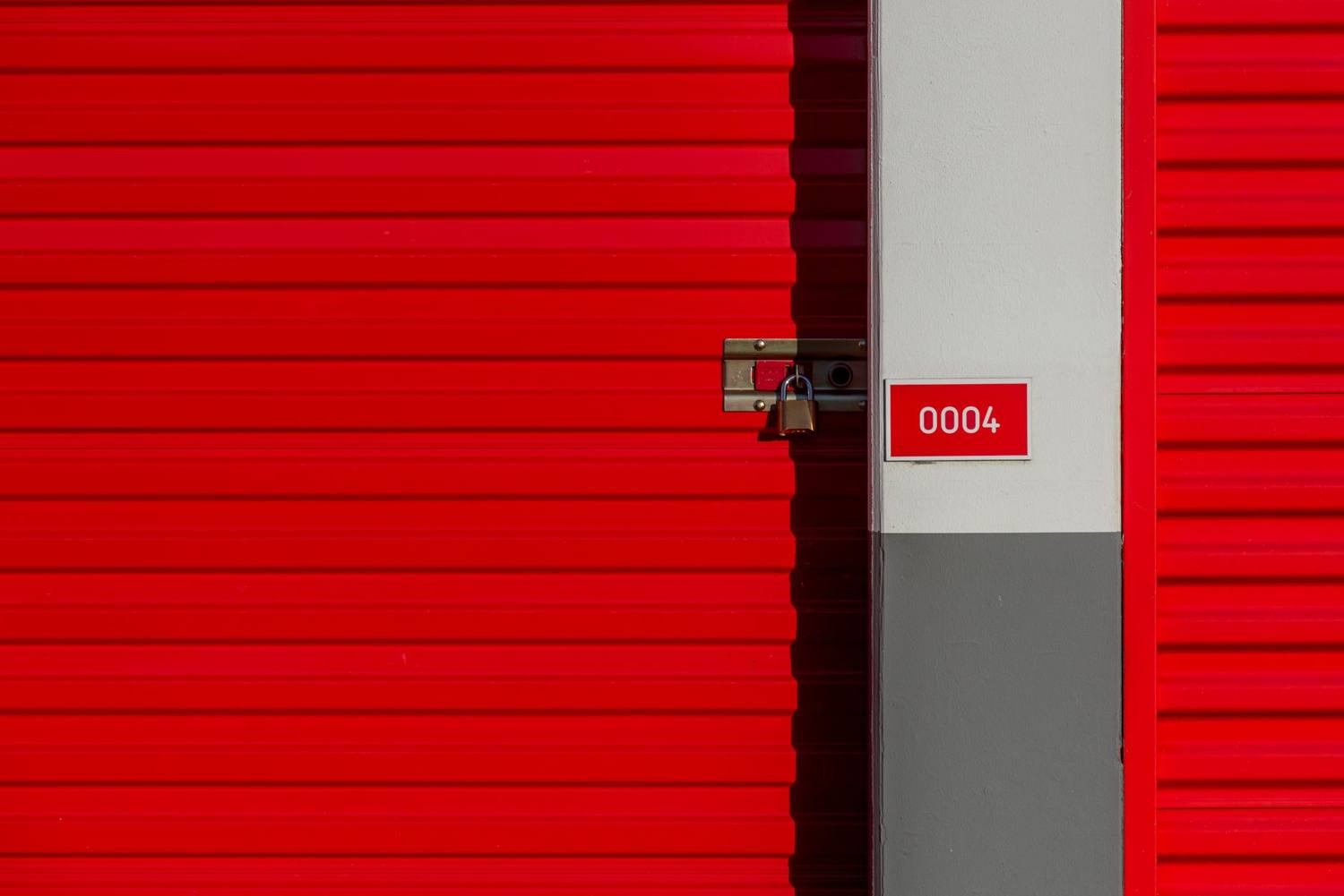 Porte d'unité de stockage en métal rouge avec cadenas et panneau blanc affichant le numéro 0004.